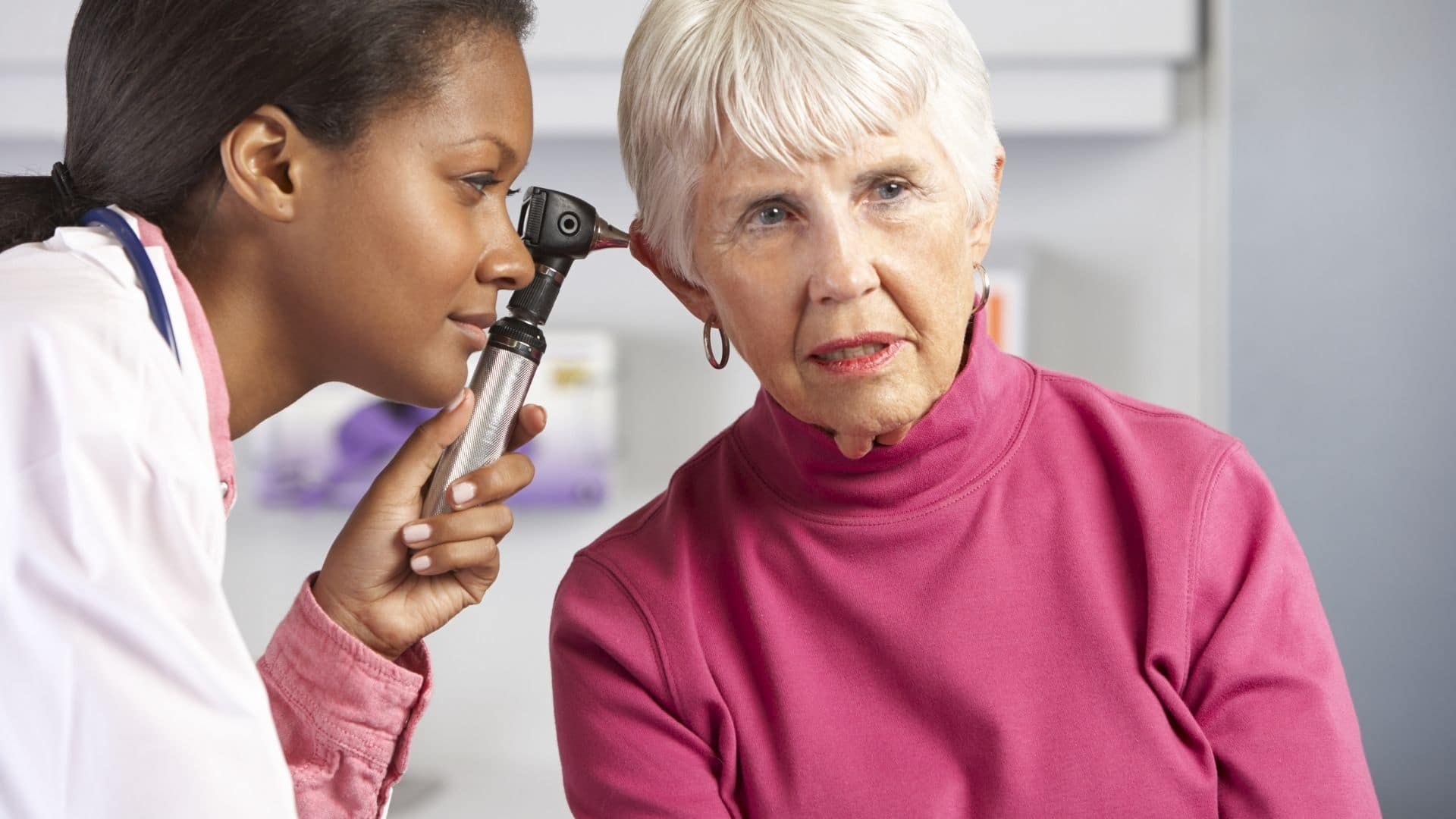 ENT specialist caring for a mature patient as she examines her ears.